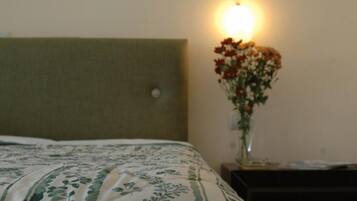 A bed with a patterned bedspread, a wall-mounted light, and a vase with flowers on a bedside table.