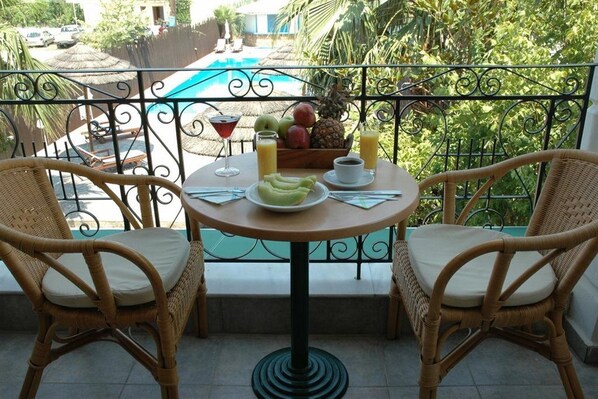 A balcony with wicker chairs, a round table with breakfast items, and a view of a swimming pool. - Santa Maura (Lefkada)