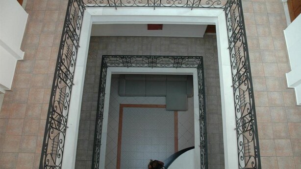 A view of a building entrance with a decorative iron gate, a tiled floor, and a door with a textured mat.