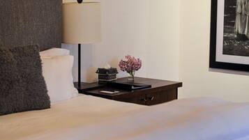 A neatly made bed with a pillow, a bedside table with a lamp, a vase with flowers, and a framed picture on the wall.