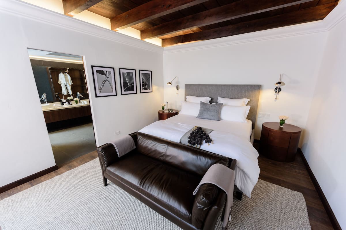 A modern bedroom with a large bed, a leather sofa, and a mirror reflecting a bathroom.