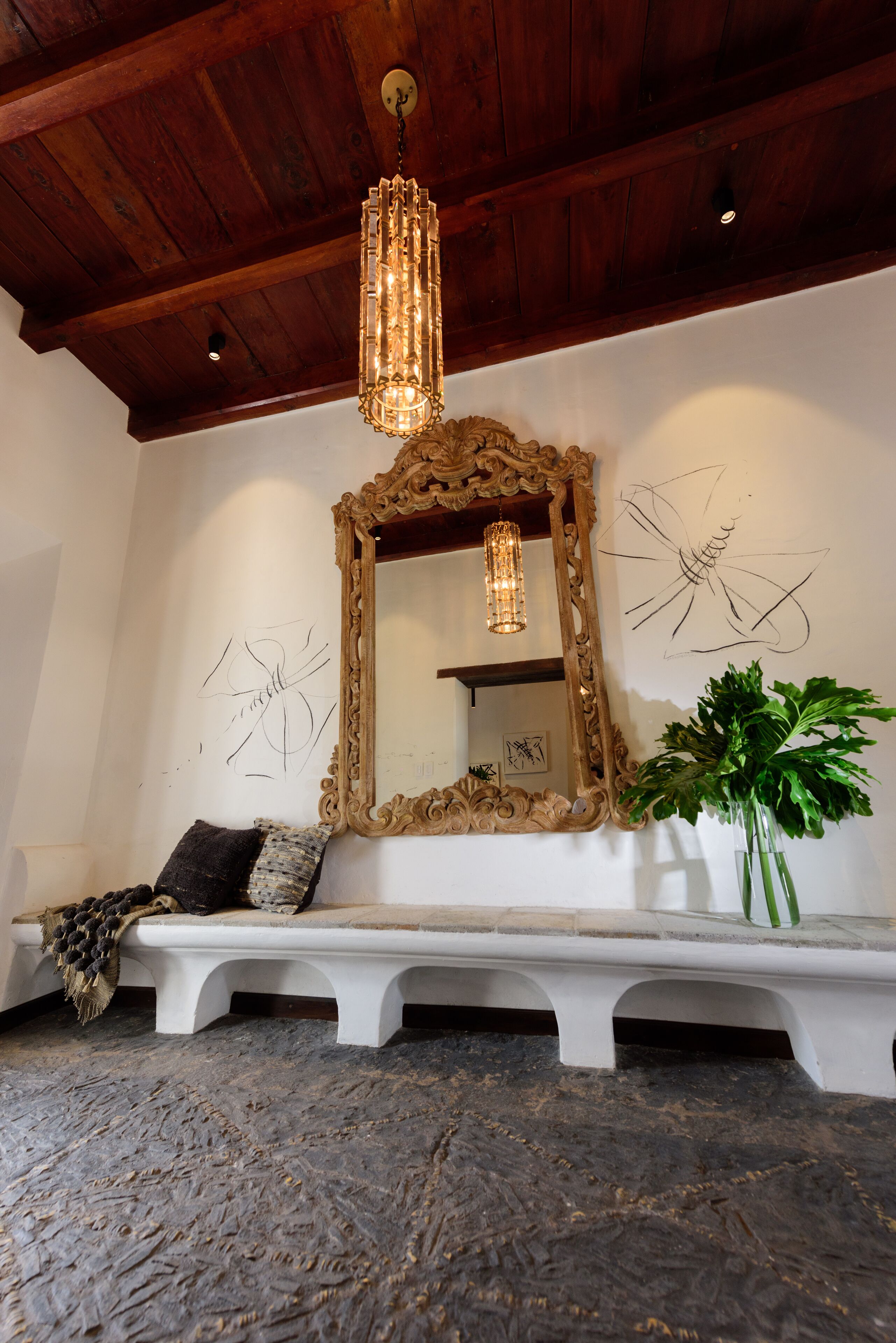 Una habitación con techo de madera, un espejo grande y ornamentado, un banco y una planta en maceta.