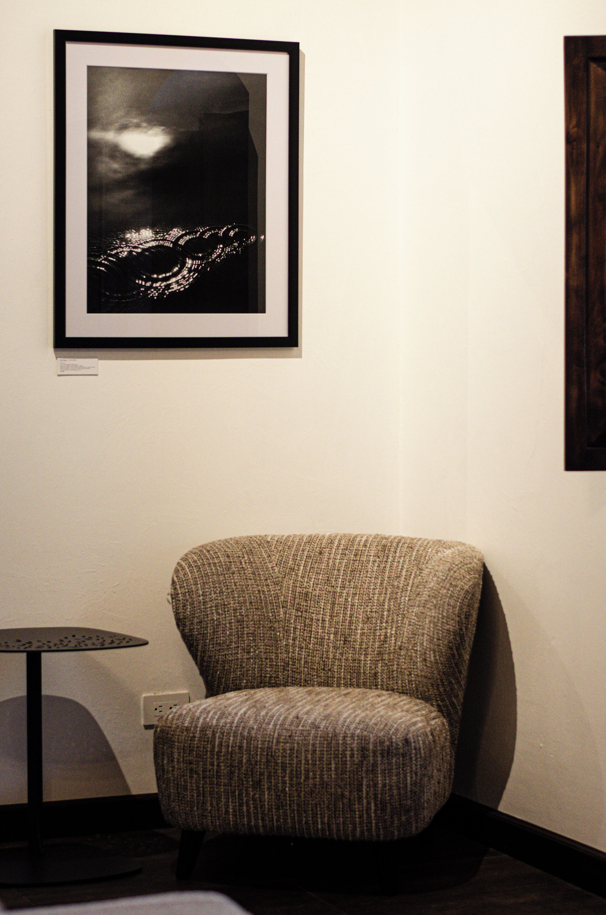 Une photographie encadrée représentant une vue nocturne d'une ville, un fauteuil à l'aspect texturé et une petite table ronde avec une lampe.