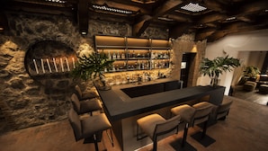 Zona de bar con pared de piedra, una barra larga y varios taburetes.
