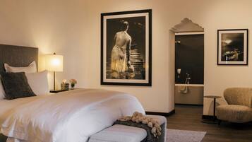 A bedroom with a large bed, a chandelier, a framed artwork, a bathtub, and a chair.