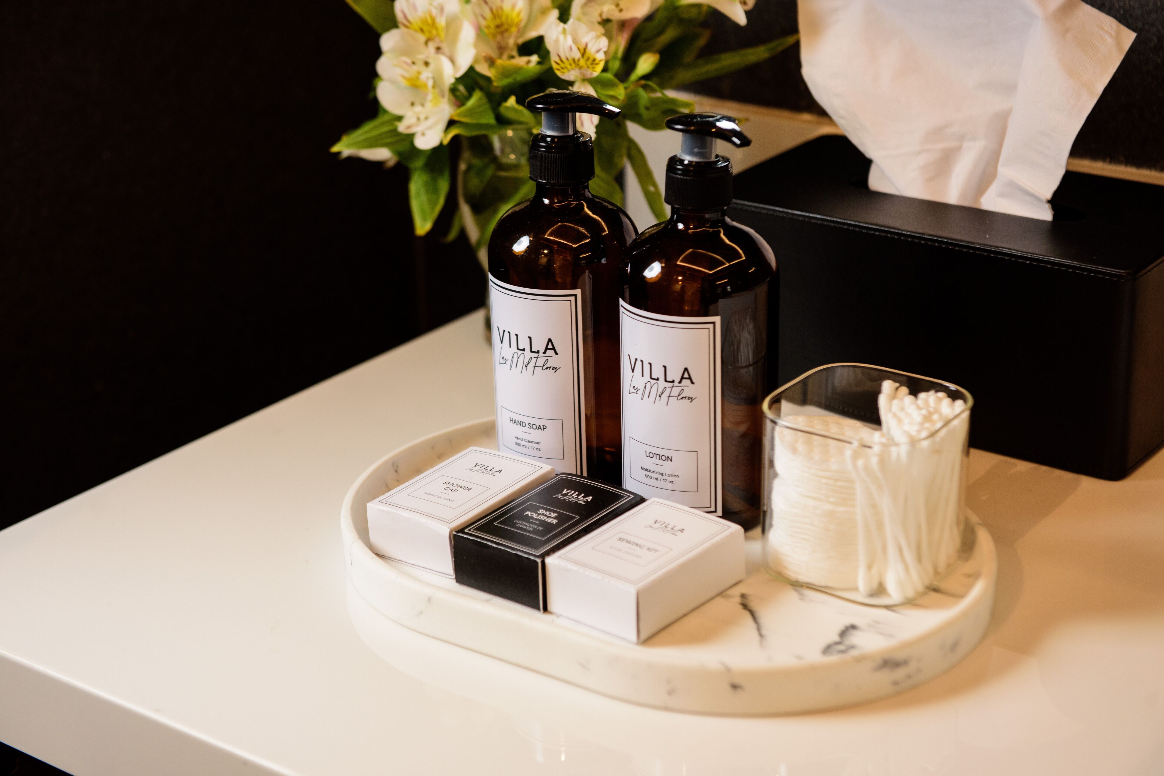 Uma bandeja com duas embalagens de sabonete líquido e loção Villa, uma caixa de gel de banho e um recipiente com cotonetes sobre um balcão de mármore.