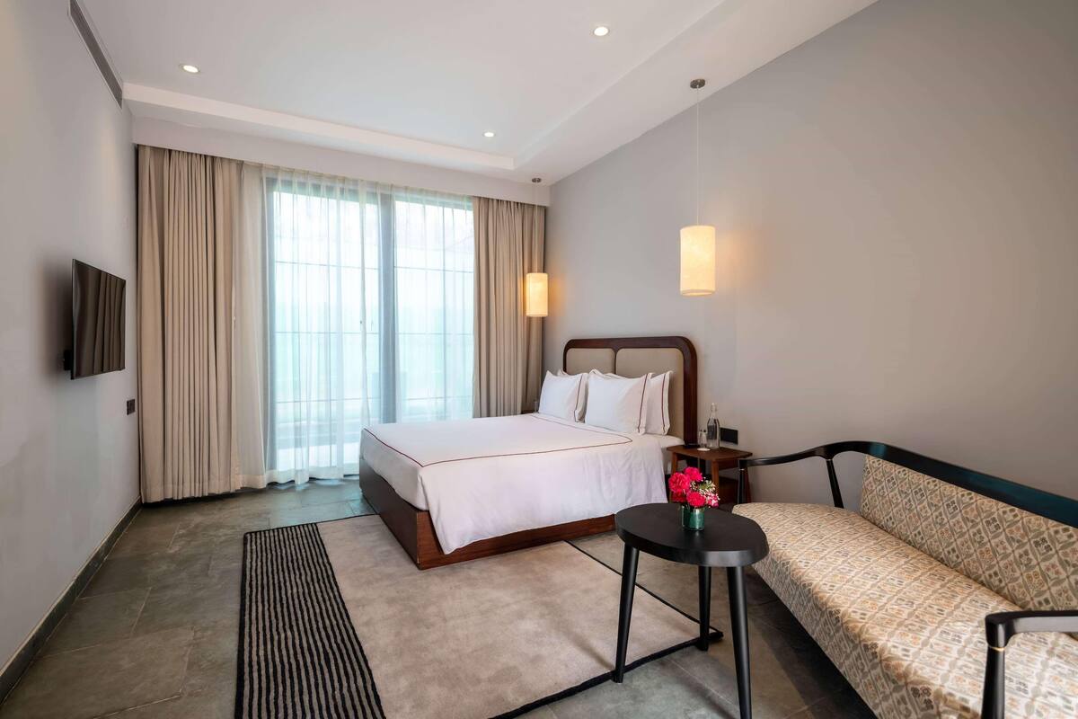 Une chambre d’hôtel avec un lit, un canapé, une petite table, une télévision et une fenêtre avec des rideaux.