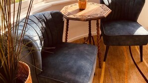 A corner seating area with a dark blue upholstered sofa, a matching chair, and a small round wooden table with a woven basket and a potted plant. - Geulzicht Hotel (Schin op Geul)