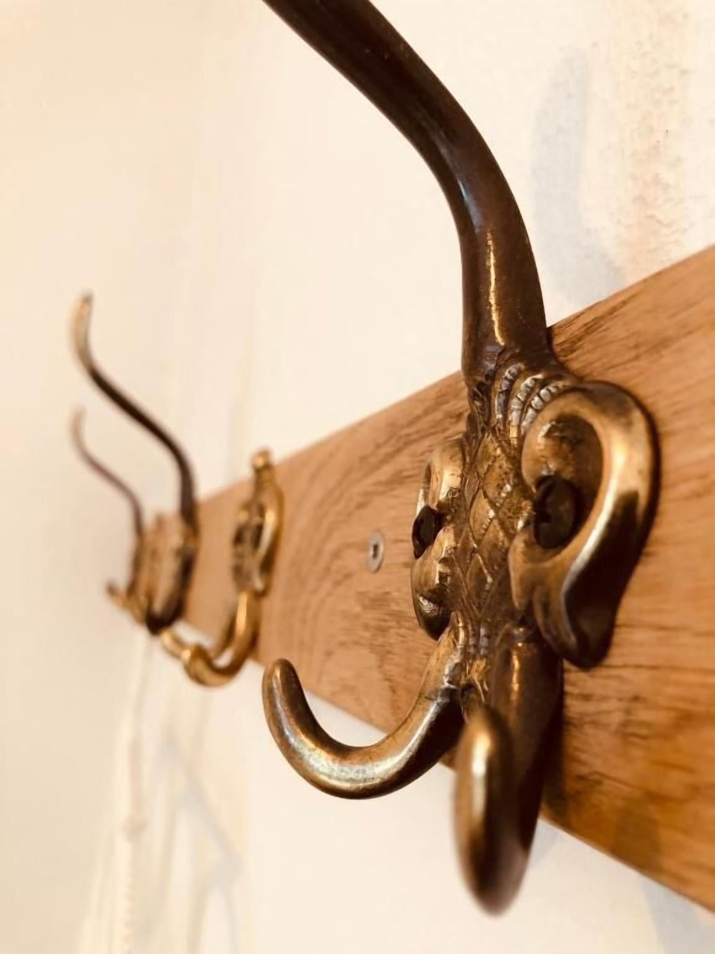 A close-up of a brass wall-mounted hook with a curved design, attached to a wooden beam.