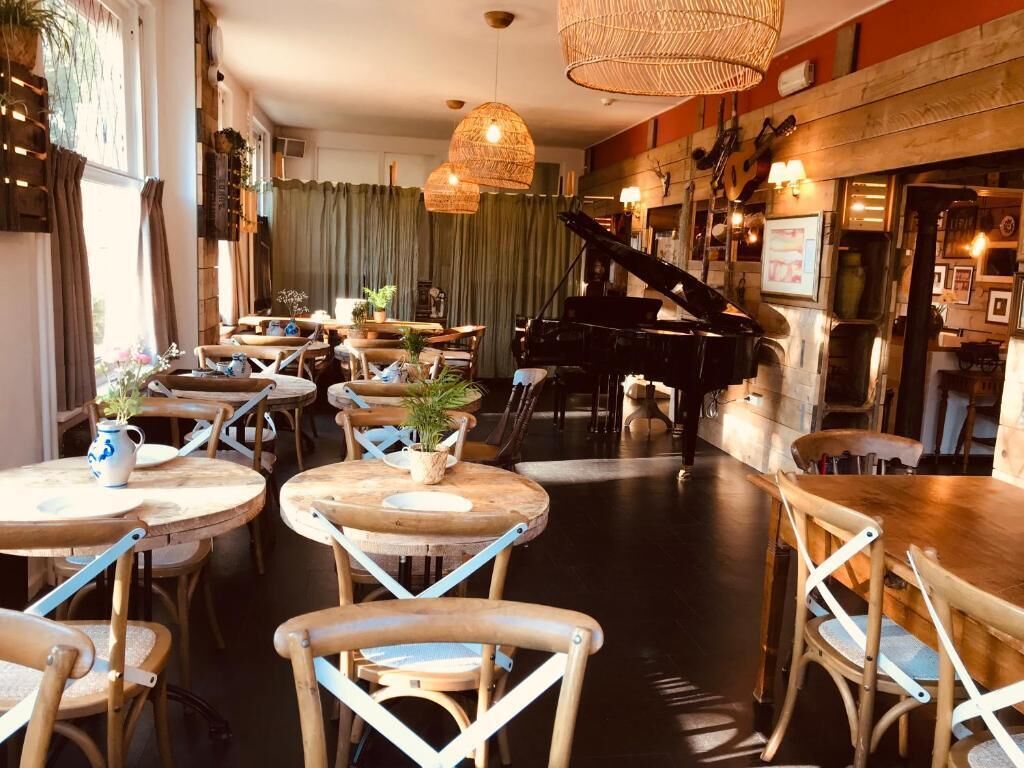A restaurant with round wooden tables and chairs, a grand piano, and hanging wicker lamps.