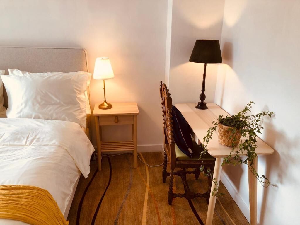 A hotel room with a bed, a desk with a lamp, a chair, and a small table with a plant.