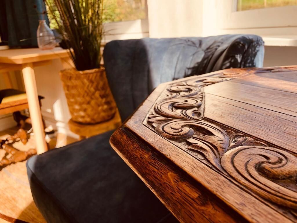 Een houten tafel met ingewikkelde gravures, een donkerblauwe stoel en een rieten mand op een houten oppervlak.