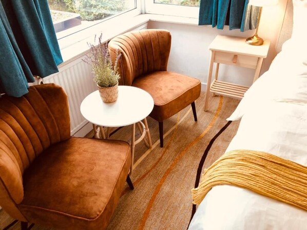 A hotel room with a bed, two brown upholstered chairs, a small round table with a potted plant, a bedside table with a lamp, and a view of the outdoors through a window. - Geulzicht Hotel (Schin op Geul)