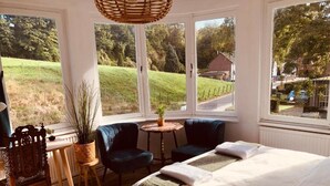 A bedroom with a large bed, two dark armchairs, a small round table, and a potted plant. - Geulzicht Hotel (Schin op Geul)