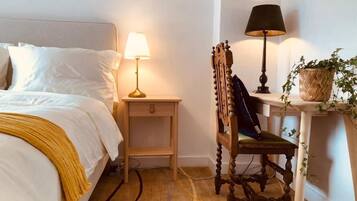 A neatly arranged bedroom with a bed, bedside lamps, a wooden chair, and a small table with a plant.