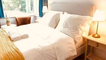 A neatly made bed with white linens, a bedside lamp, and a view of the outdoors through a window.