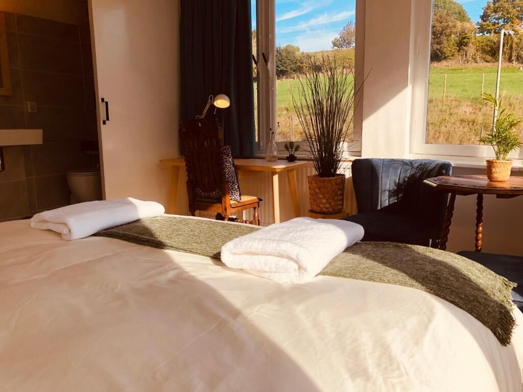 Et hotelværelse med en stor seng, et skrivebord, en stol, en lampe og udsigt til det fri.