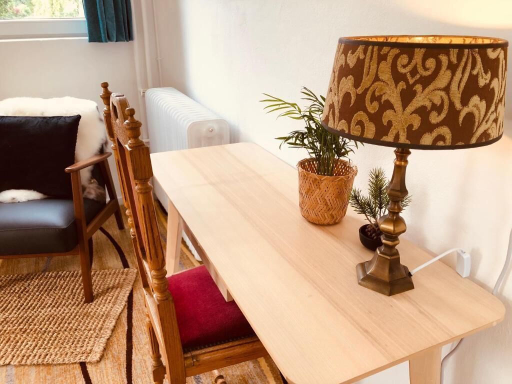 Una mesa de comedor de madera con una lámpara, una cesta tejida con plantas y un cojín rojo en una silla.