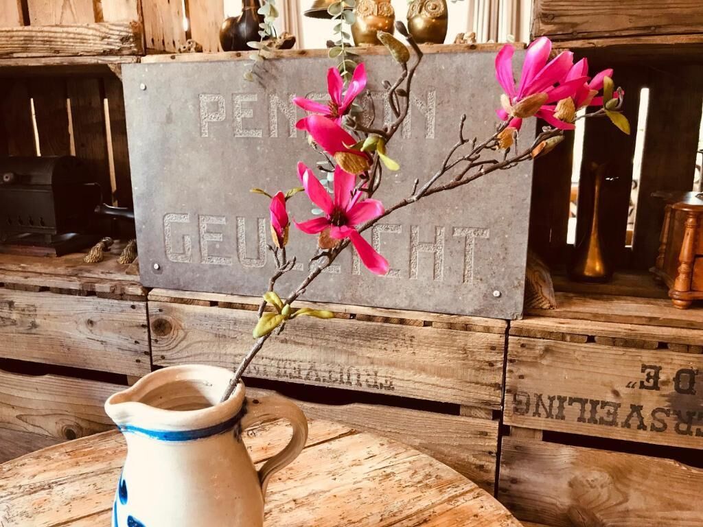 A rustic wooden table with a ceramic pitcher and a branch of pink flowers.