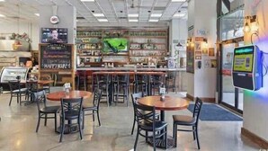 Un restaurante con zona de bar, diversas opciones de asientos que incluyen mesas redondas y sillas, y un panel de menú a la vista.