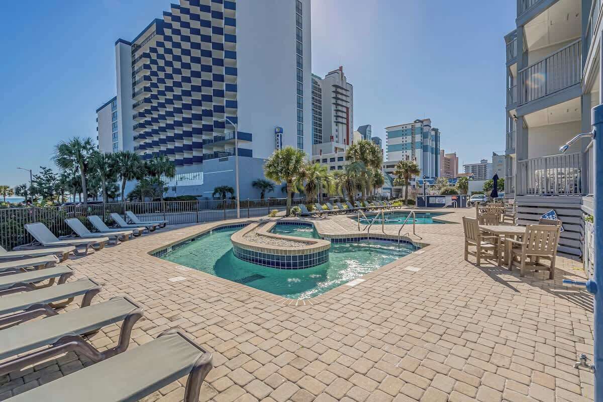 A rooftop pool area with lounge chairs, a hot tub, and a dining area.