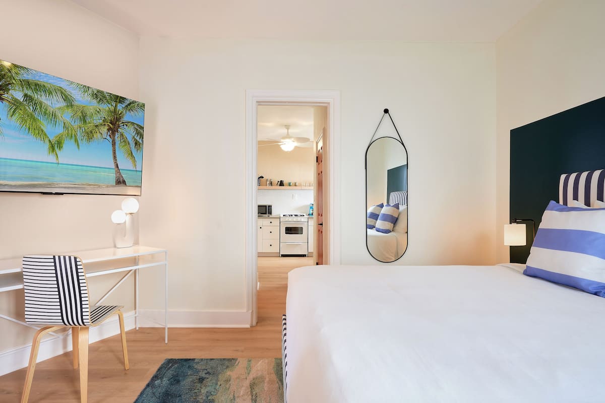 Habitación de hotel con cama, escritorio, silla, espejo y un cuadro de una playa.