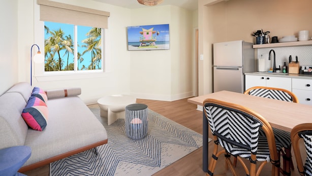 A modern living room with a sofa, a dining table with chairs, a small stool, and a kitchen area with a refrigerator and shelves. - Pantera Rosa (Miami Beach)