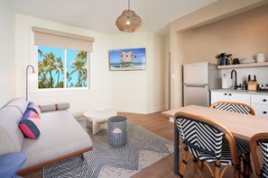 A modern living room with a sofa, a dining table with chairs, a small stool, and a kitchen area with a refrigerator and shelves. - Pantera Rosa (Miami Beach)
