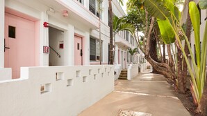 A narrow, tree-lined street with white buildings featuring pink doors and windows. - Pantera Rosa (Miami Beach)