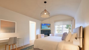 A spacious bedroom with a large bed, a desk, a chair, a TV, and a window with a view of palm trees. - Pantera Rosa (Miami Beach)
