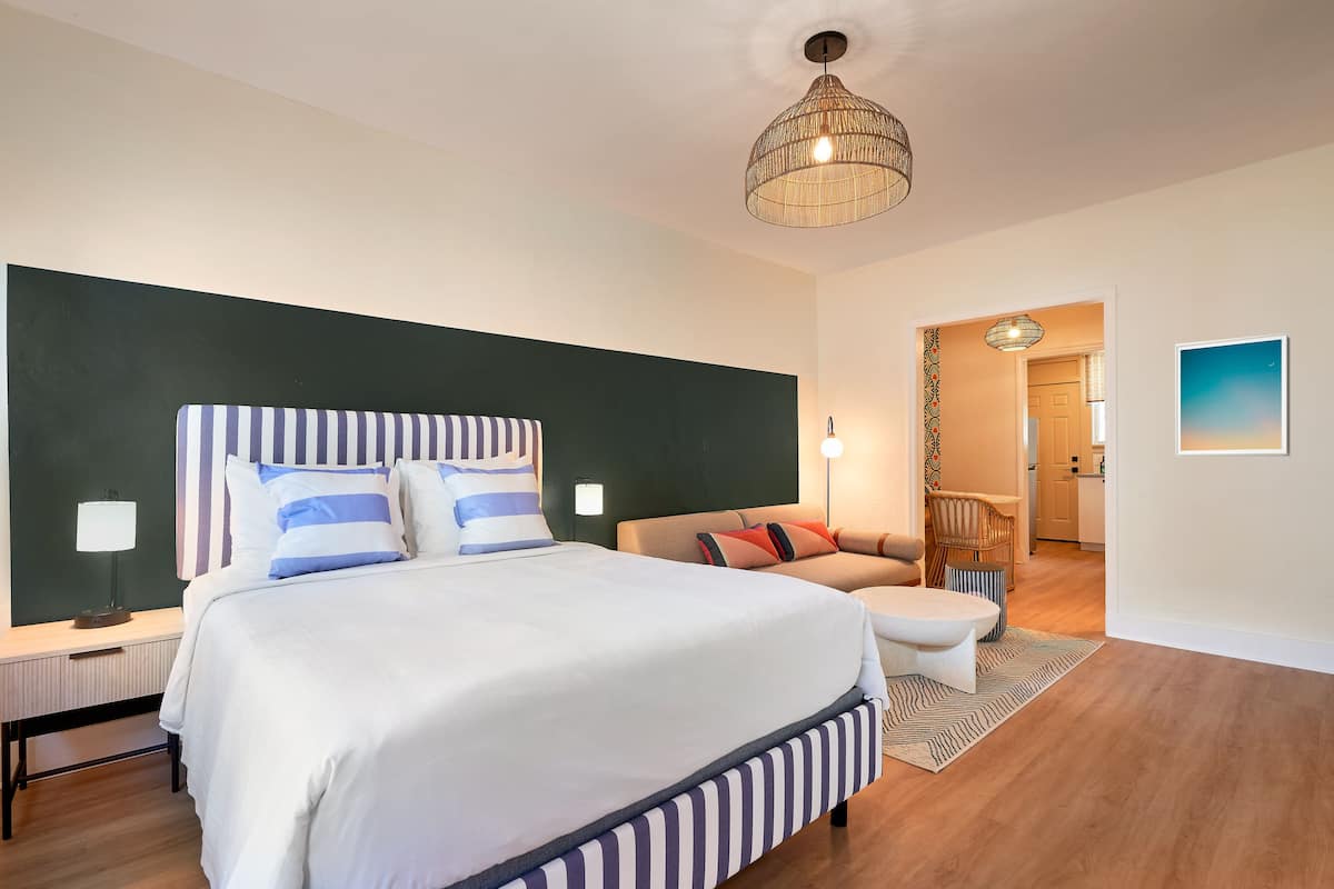Un dormitorio moderno con una cama grande, mesitas de noche, una lámpara colgante, un sofá y una alfombra estampada.
