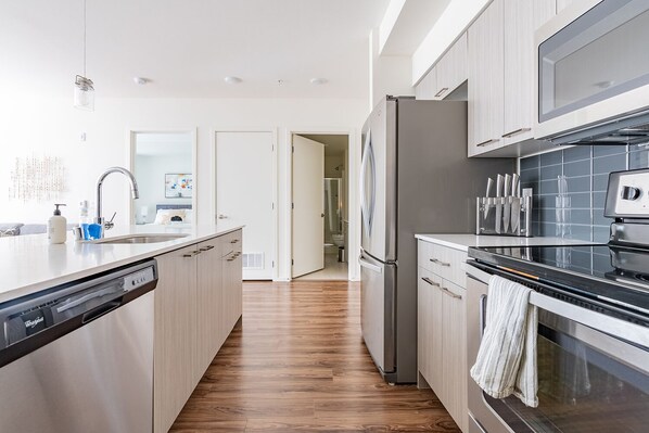 A modern kitchen with a dishwasher, stainless steel appliances, and a wooden floor.