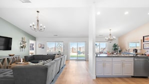 A spacious living room with a grey sectional sofa, a flat-screen TV, and a chandelier. - ✨Amazing Views✨Backyard Trails 🏜️Close to National Park, Shops, Restaurants ☕️ (Joshua Tree)