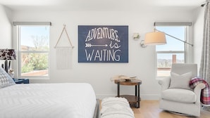 A bedroom with a bed, a chair, a small table, and a wall sign. - ✨Amazing Views✨Backyard Trails 🏜️Close to National Park, Shops, Restaurants ☕️ (Joshua Tree)