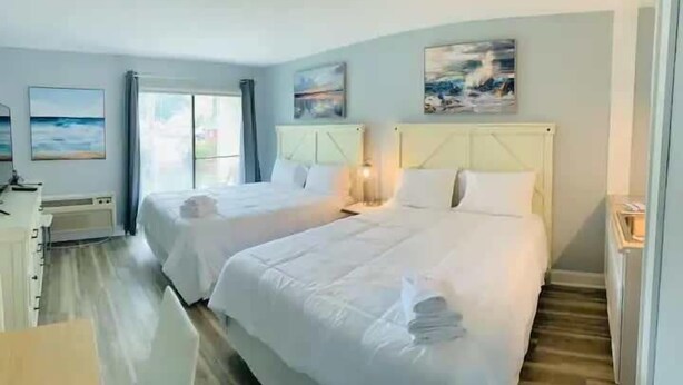A hotel room with two beds, a desk, and artwork on the walls.
