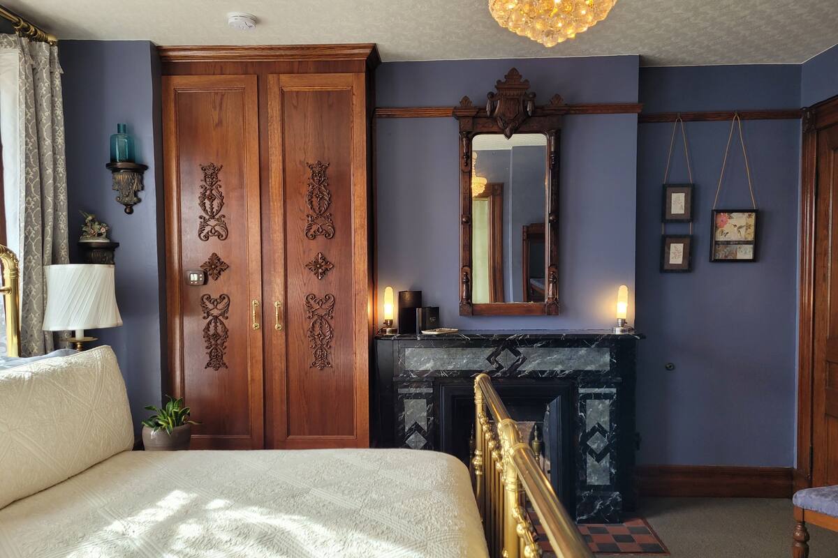 Quarto com uma cama grande, um guarda-roupa de madeira, lareira e um espelho na parede.