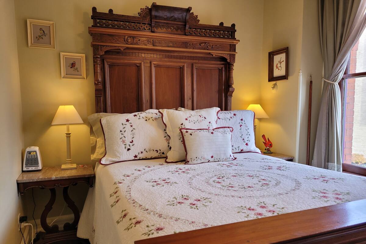 Cama bem arrumada com roupa de cama floral, cabeceira de madeira e duas luminárias laterais.