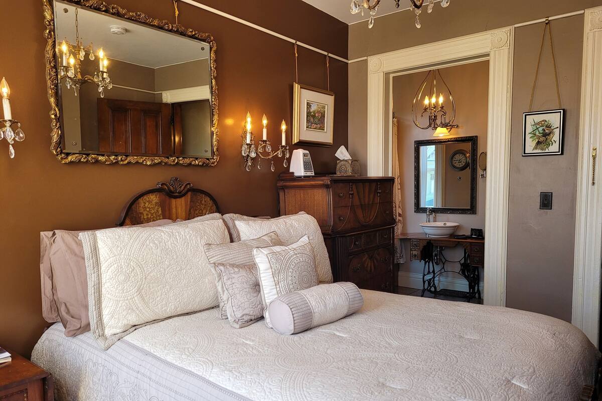 Quarto com uma cama grande, cômoda, penteadeira com espelho e lustre.