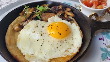 A skillet with a fried egg, mushrooms, and greens on a table.