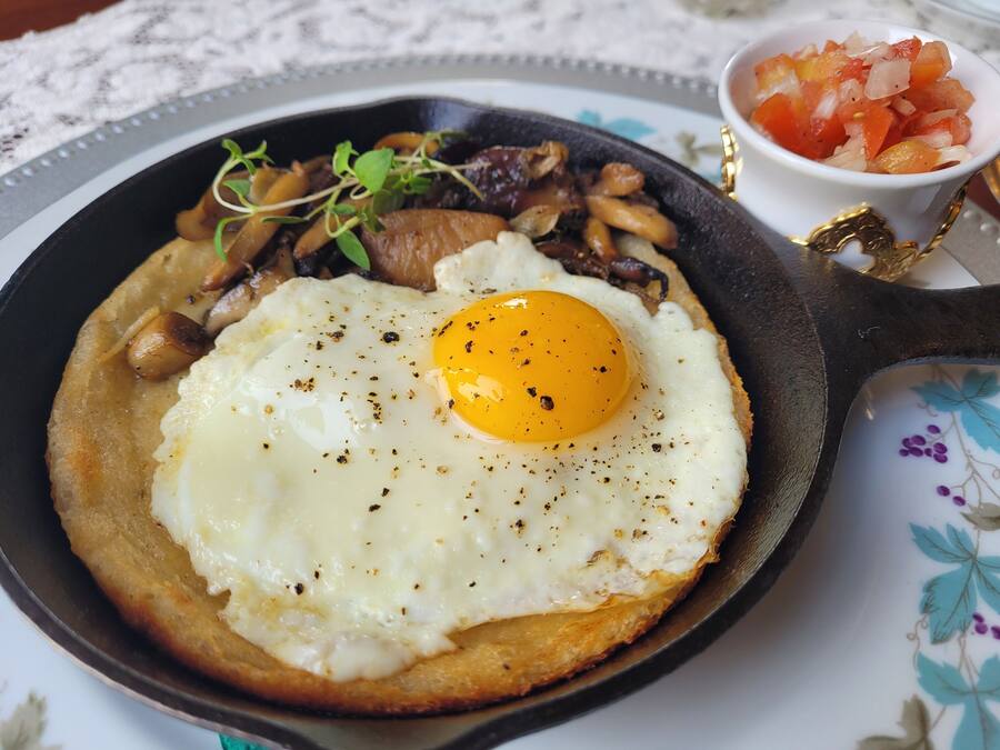 A skillet with a fried egg, mushrooms, and greens on a table.