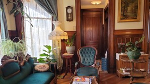 Un salon traditionnel avec un canapé vert, une table basse en bois sur laquelle sont posés des livres, un fauteuil bleu et diverses plantes en pot.