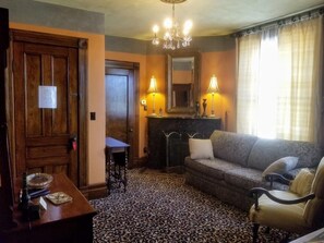 A room with a patterned carpet, a wooden door, a sofa, a small table, and a chandelier. - Buffalo Harmony House (Buffalo)
