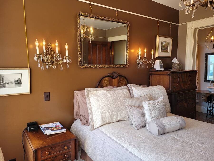 A bedroom with a large bed, ornate mirror, wall sconces, and a dresser.