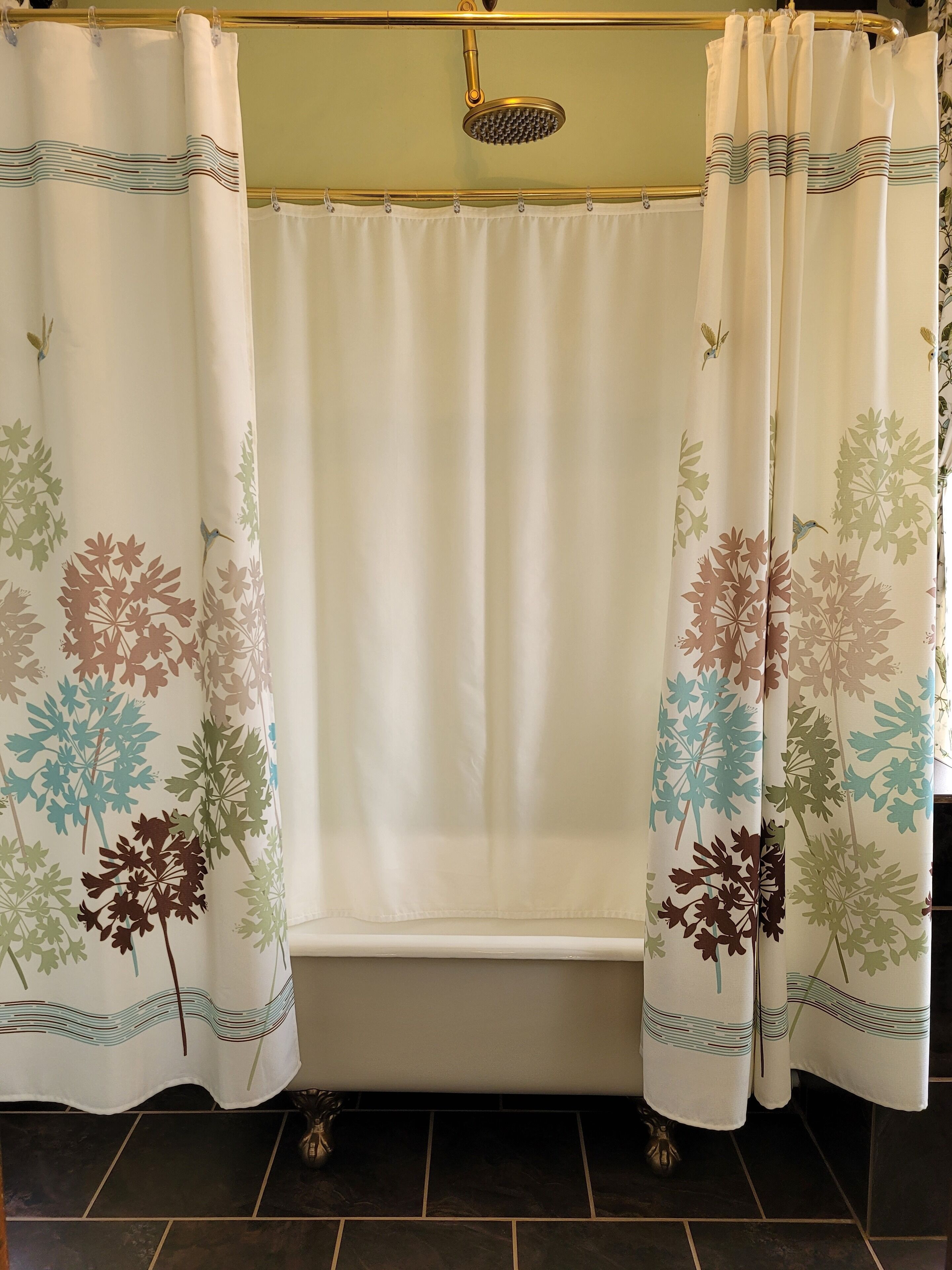 Un baño con una bañera, dos cortinas de ducha con motivos florales y un cabezal de ducha.