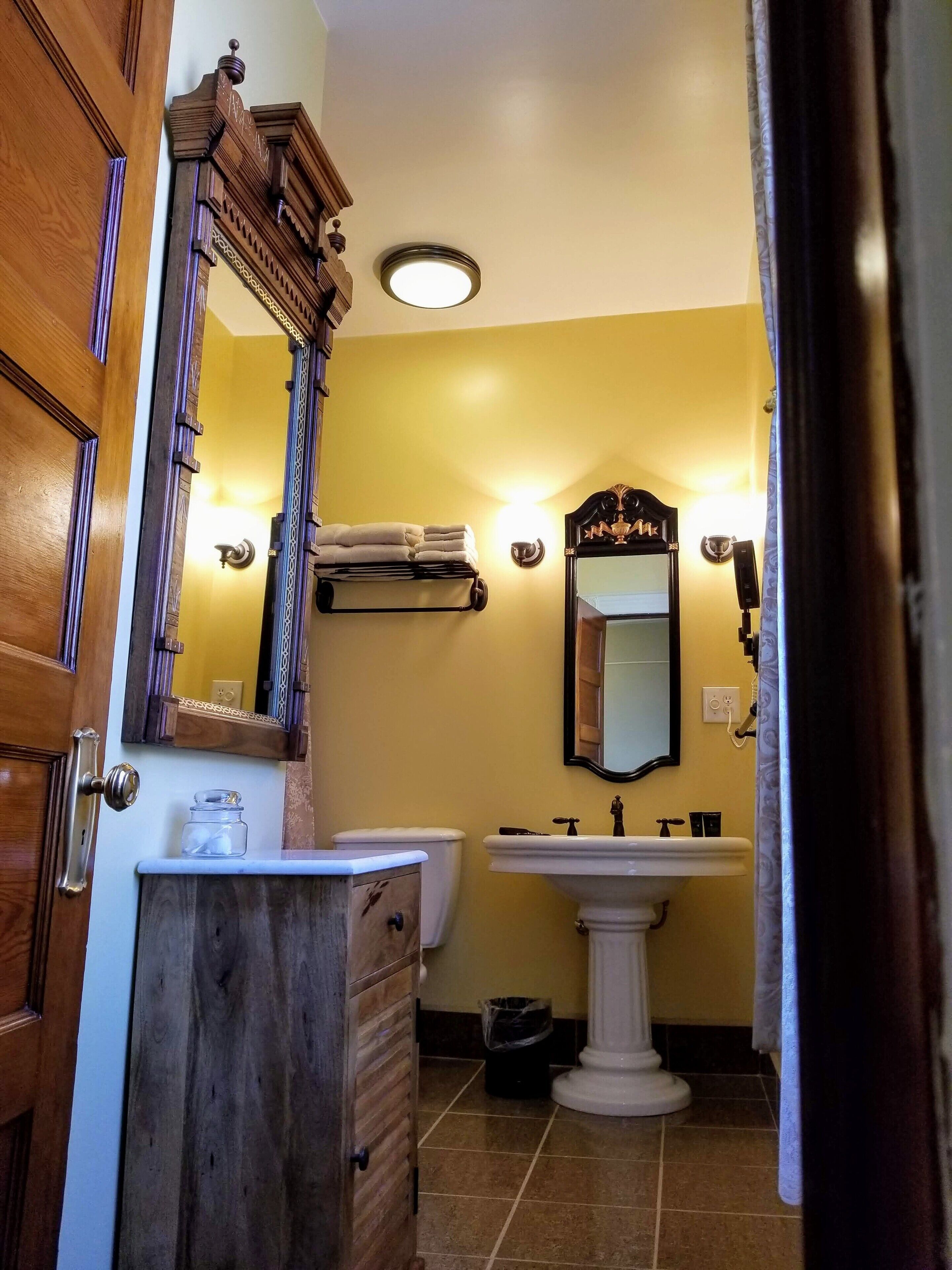 Een badkamer met een houten wastafelmeubel, een zuilwastafel, een toilet en een spiegel.