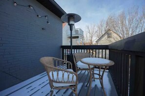 Un balcon avec des fauteuils en osier et une table, une guirlande lumineuse et une rambarde en métal.