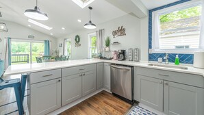 A modern kitchen with grey cabinets, a dishwasher, and a large window with a view of greenery. - Private Waterfront Home Nestled In A Quiet Section Of Lake Hopatcong (Jefferson)