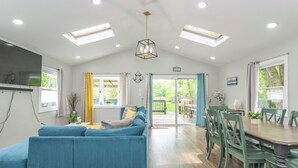 A spacious living area with a blue sofa, a dining table with chairs, and a kitchen area with a hanging light fixture. - Private Waterfront Home Nestled In A Quiet Section Of Lake Hopatcong (Jefferson)