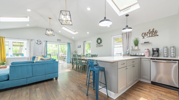 A spacious kitchen with a central island, a dining area with chairs, a blue sofa, and a kitchen island with bar stools. - Private Waterfront Home Nestled In A Quiet Section Of Lake Hopatcong (Jefferson)