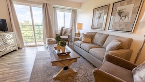 A living room with a sofa, armchair, coffee table, and a TV. There are two framed pictures on the wall, a lamp, and a window with curtains. - Mountaintop condo with indoor and outdoor pools (Gatlinburg)